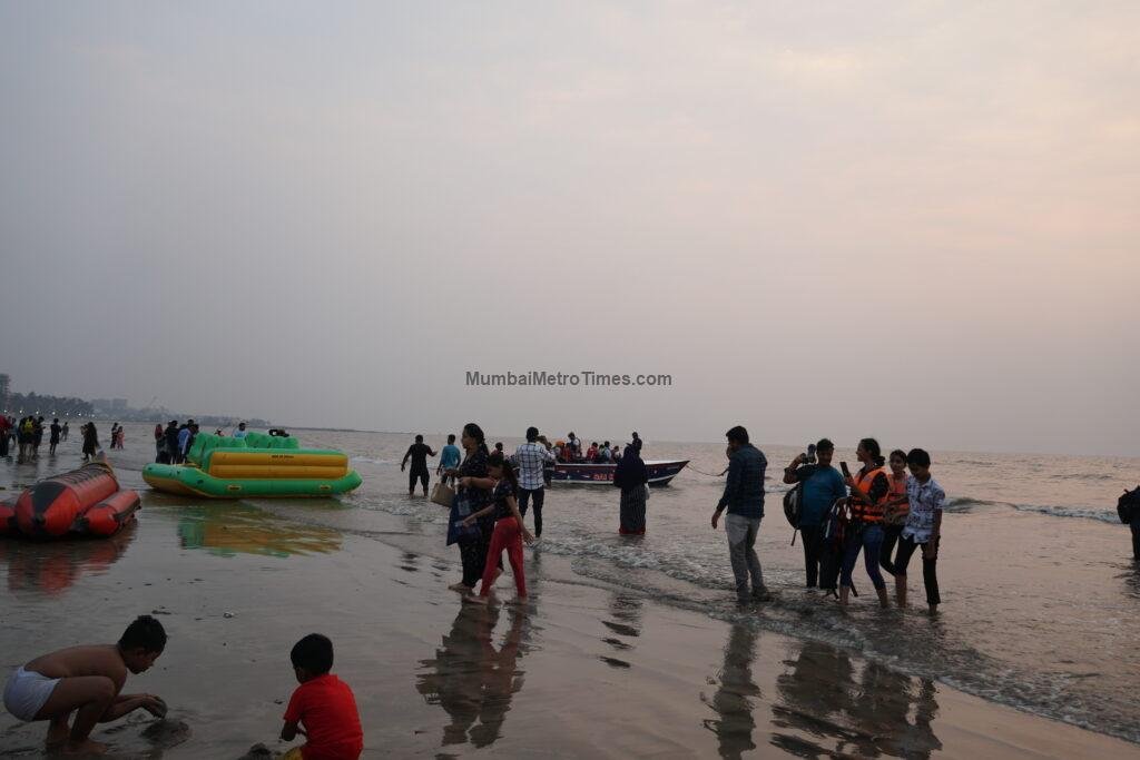 Visitors at the water's edge on Juhu Beach with boats on the sand